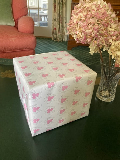 A large square present is wrapped in Sharing A Big Heart wrapping paper. The gift is placed near a vase with hydrangea flowers.