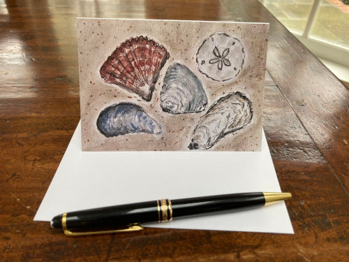 A mockup of the front of the card atop a wooden table with the envelope and a black fountain pen,