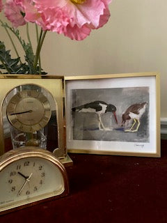 Mockup on a burgundy velvet topped desk with 2 gold clocks and pink poppies in a vase. The print is in a small gold frame with white matte.