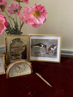 Mockup of Shore Birds sitting on a red velvet desk and surrounded by three gold clocks and pink poppies in a vase.