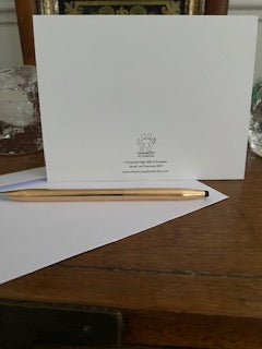 Back of the Snowball Fight With A Snowman greeting card displayed upright on brown desktop with white envelope and gold pen.