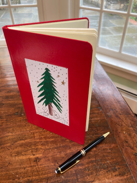 Mock up of Under The Tree journal in red is set on a table with its pages fanned open.