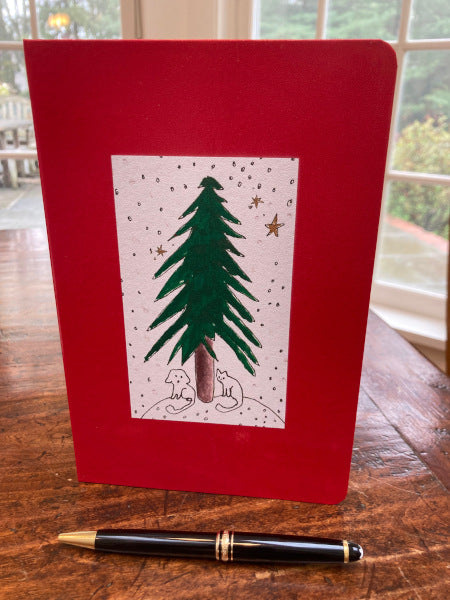 Mock up of the red journal Under The Tree is set on a wooden table with a fountain pen. The colors on the journal and adorable painting complement each other wonderfully.