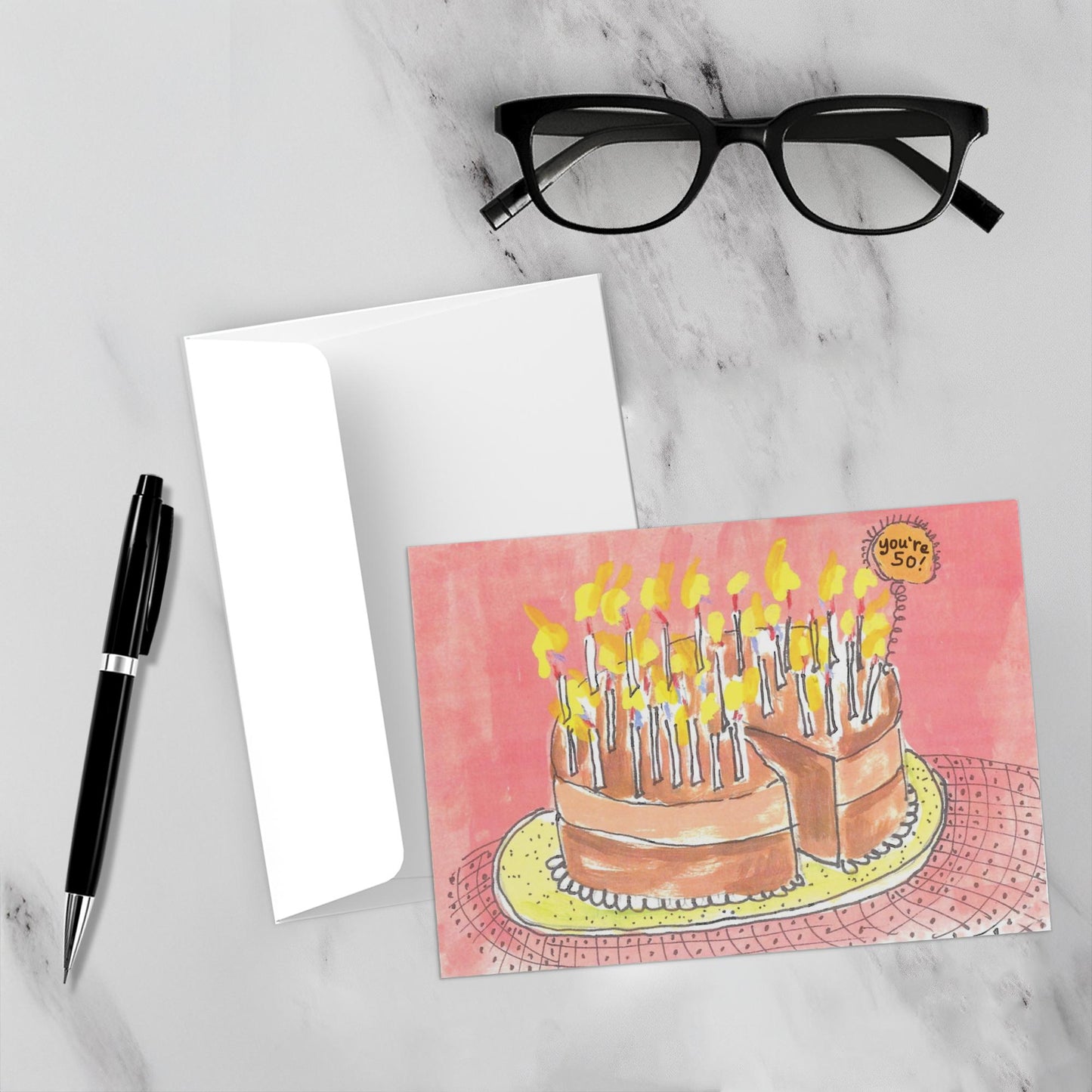 The front of the birthday card along with its envelope are displayed on a white marble background with a pen and reading glasses.