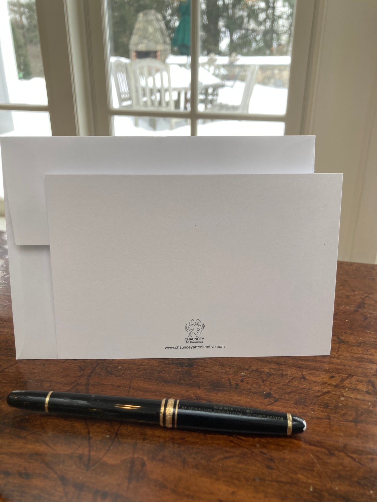 Back of Happy Trails flat note card with it's envelope on a wooden table in front of a window with a snowy background.