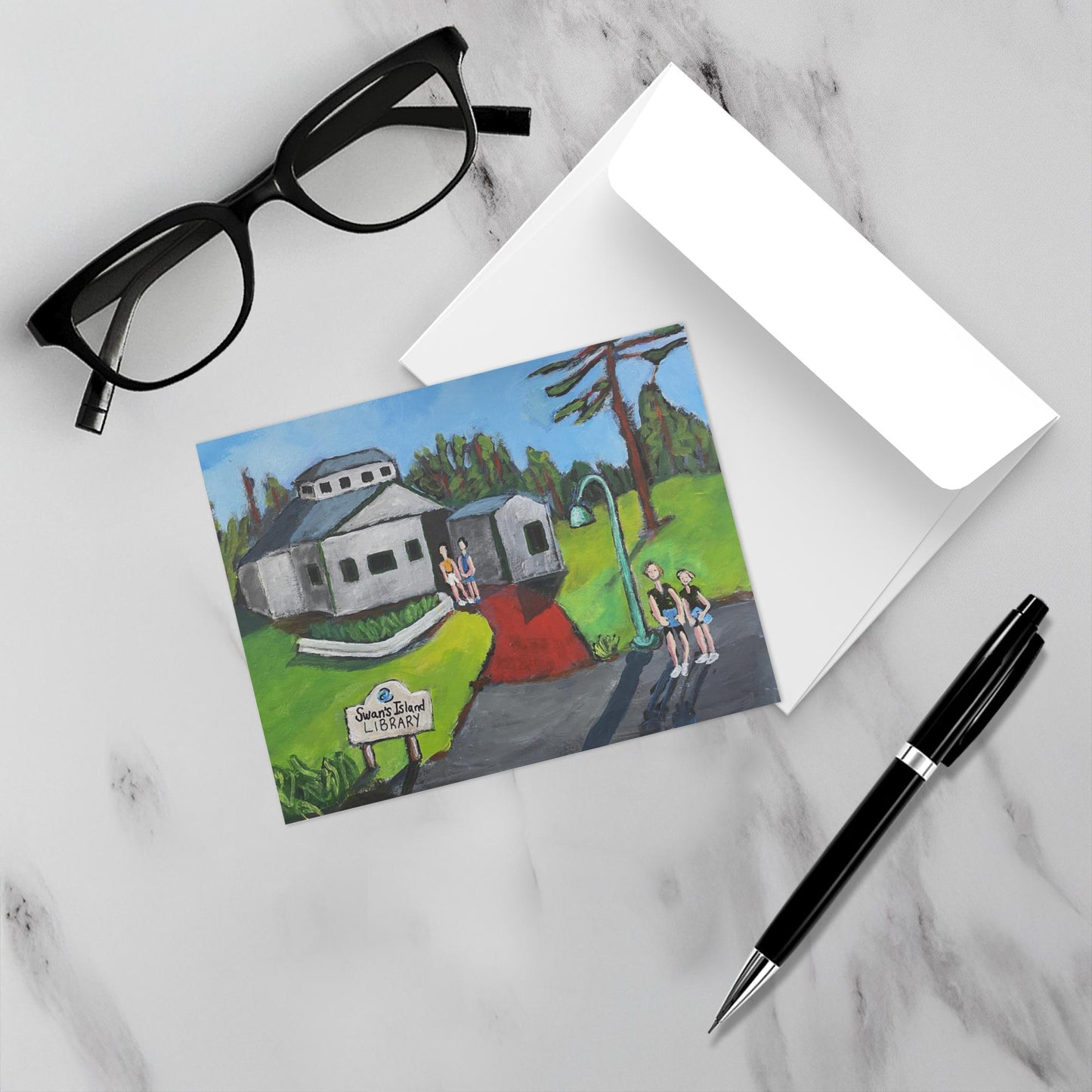 Island Chapters Swan's Island greeting card shown on a marble surface wit its envelope, eyeglasses and a pen.