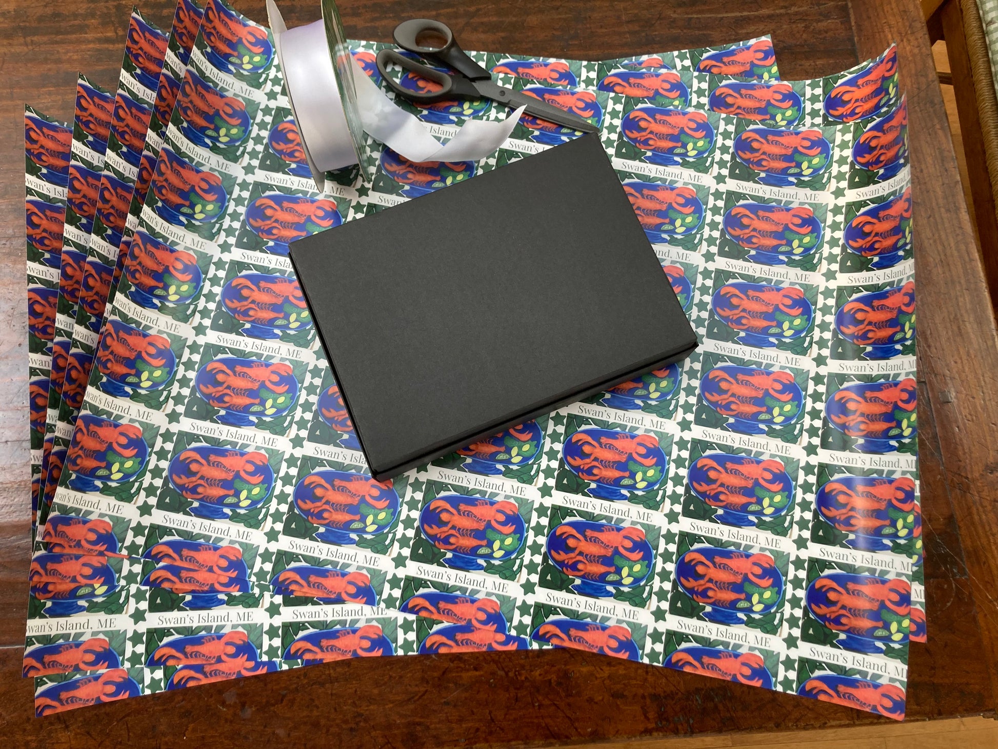 Mock up of gift about to be wrapped in Swan's Island Lobster double sided wrapping paper, 5 sheets shown.