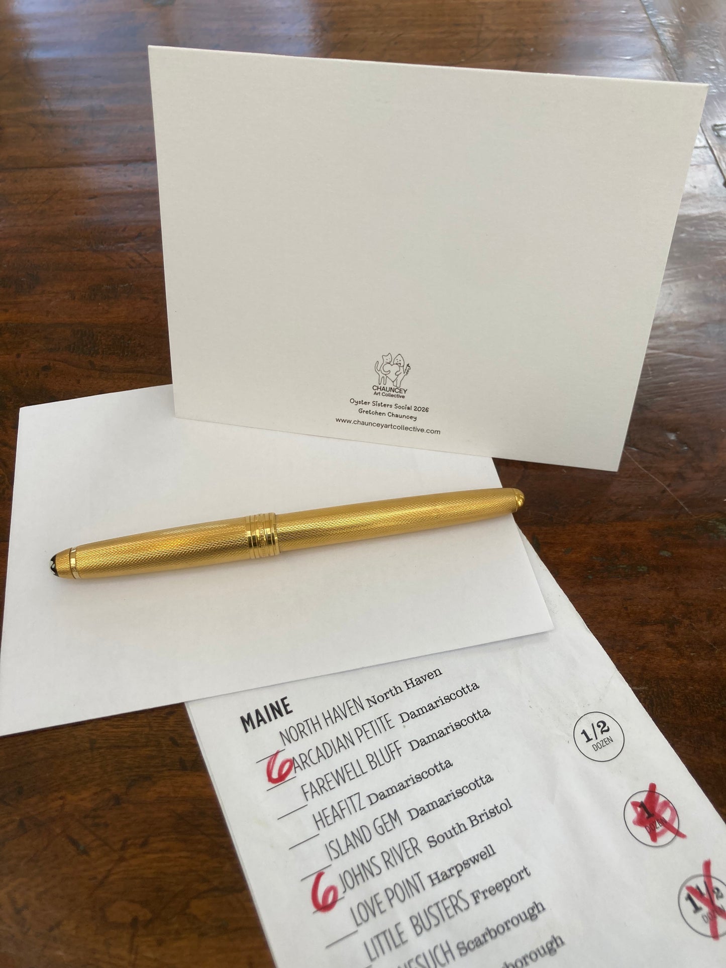 Gold pen on a an envelope with back of Oytser Sisters Social card offered by Chauncey Art Collective.