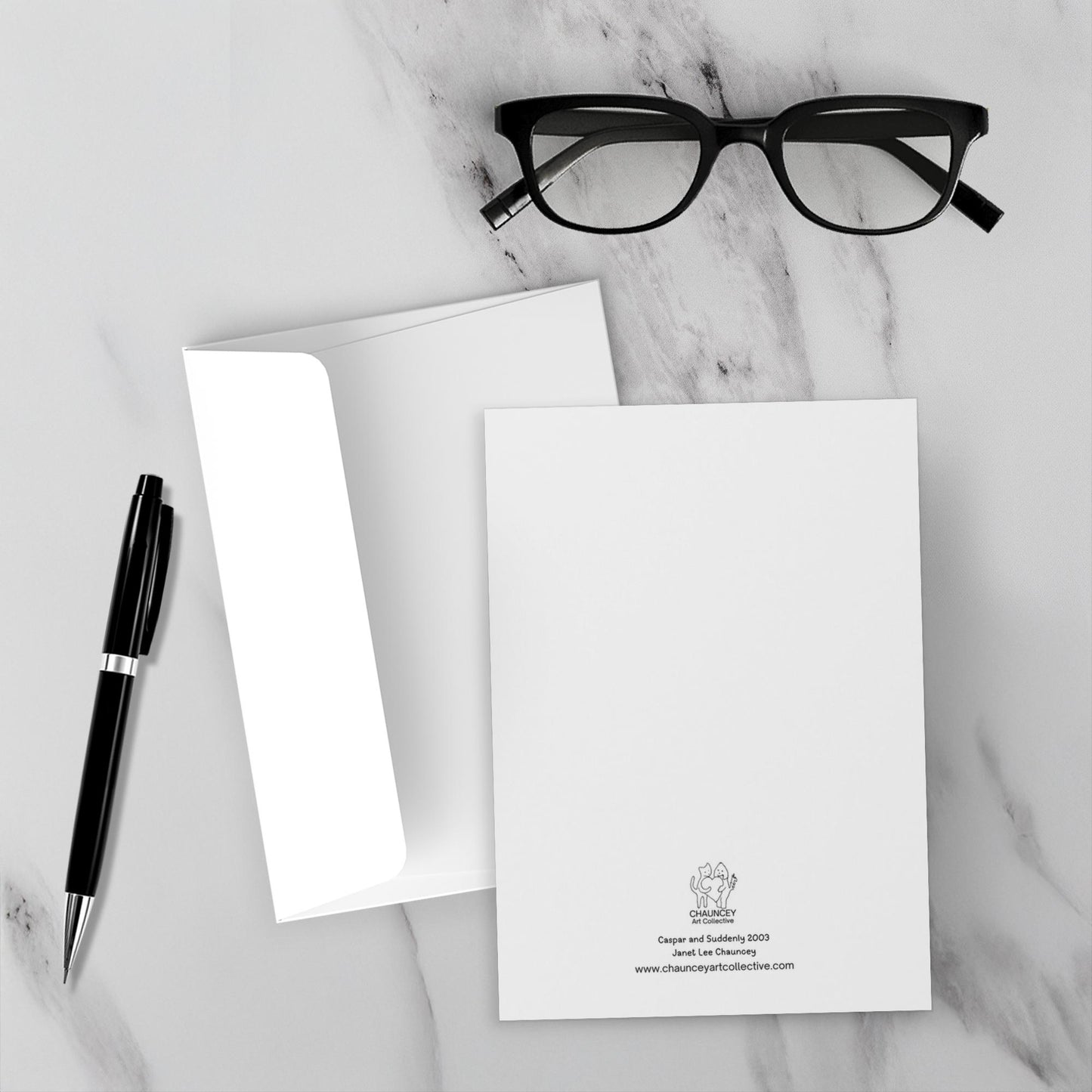 The backside of Caspar and Suddenly Greeting card with the title and Chauncey Art Collective logo. Displayed on a marble surface with a black pen and eyeglasses.