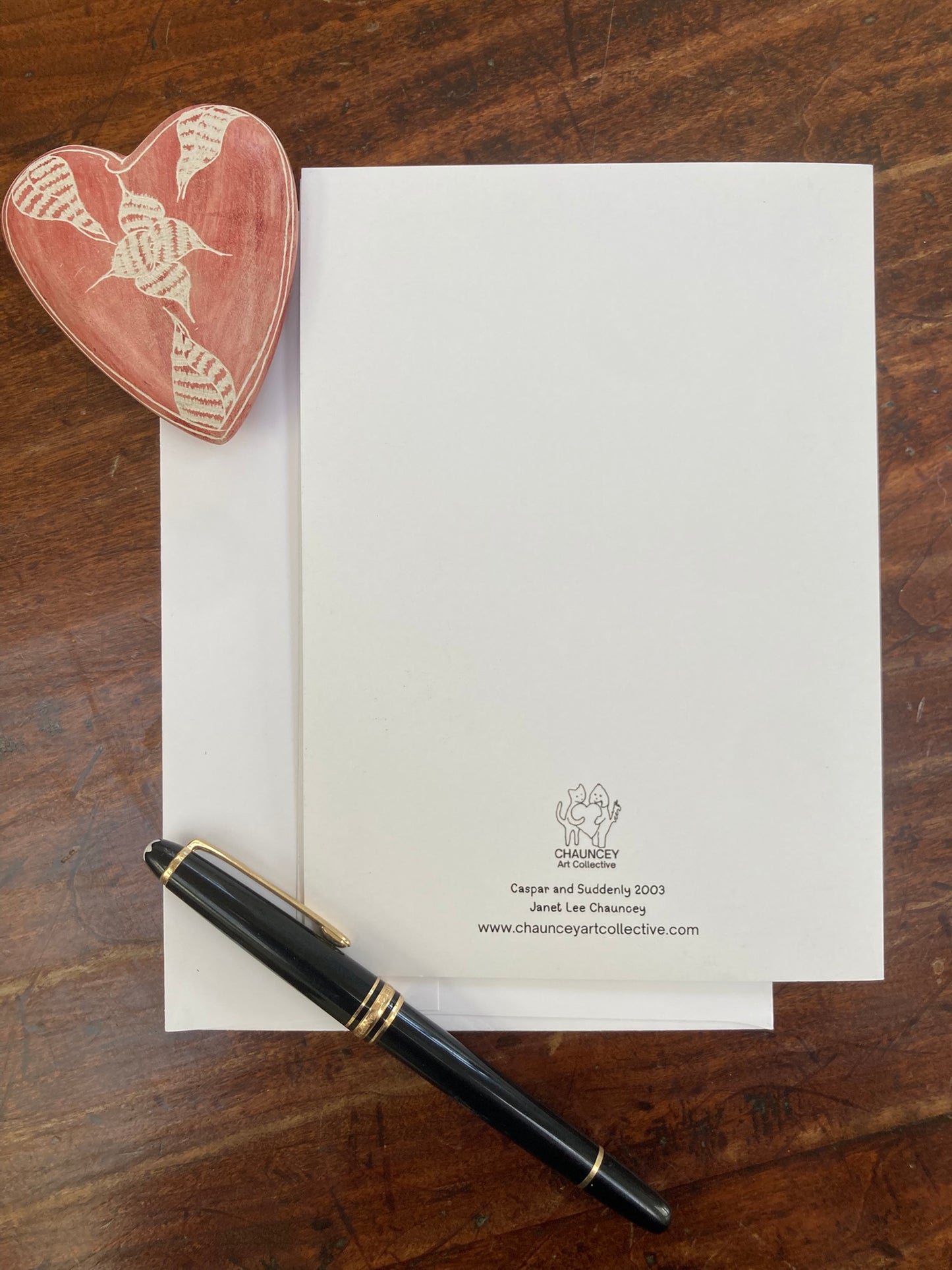 Heart-shaped object, pen, and letter on a wooden surface with 'Chauncey Art Collective branding.