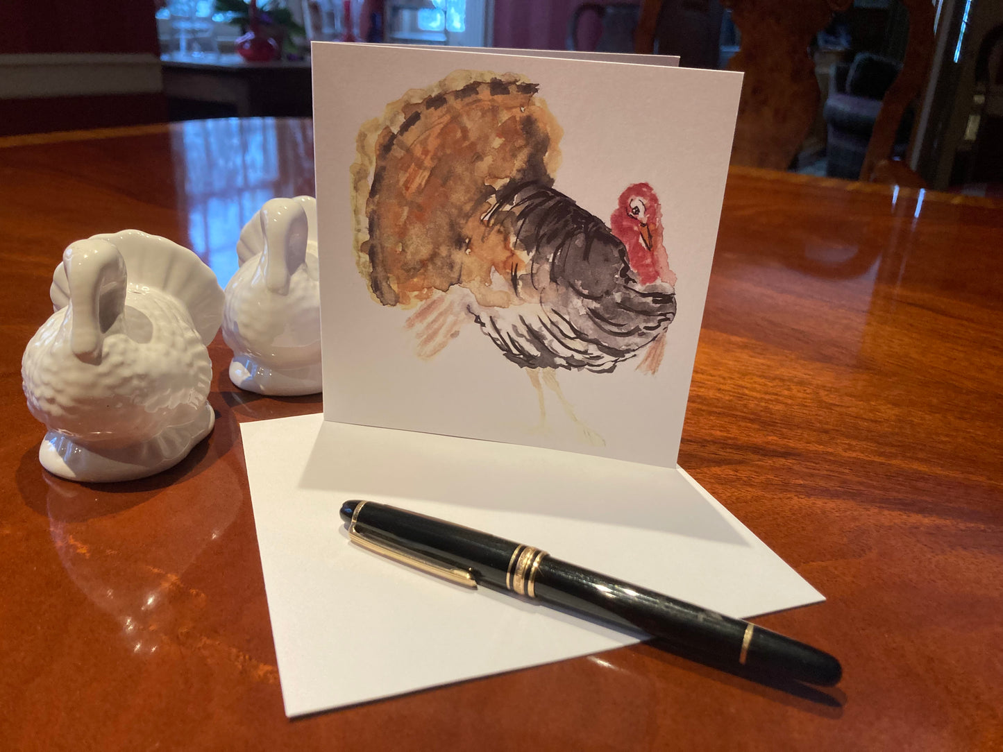 Card with a turkey illustration on a wooden table with a pen and decorative items.