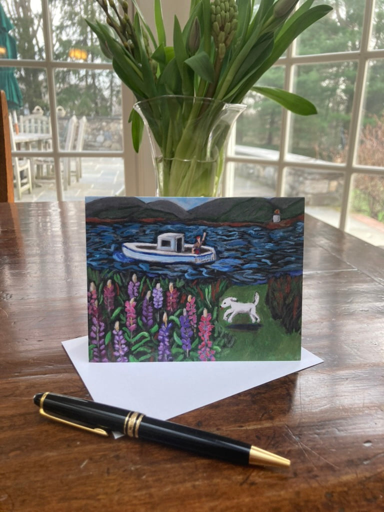 Greeting card with a boat and dog illustration on a wooden table with flowers and a pen.