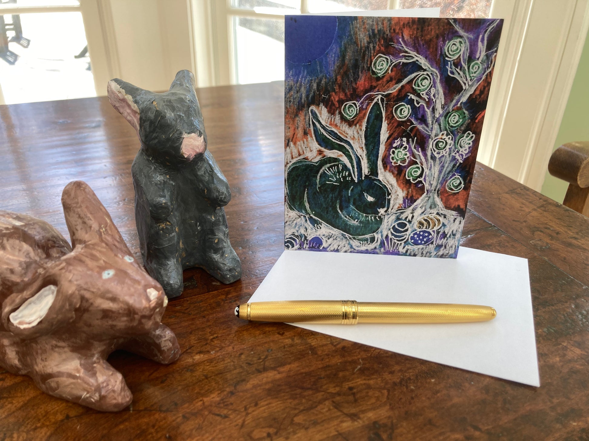 Decorative rabbit figurines with the Bold Bunny card with art work by Janet Lee Chauncey on a wooden table.