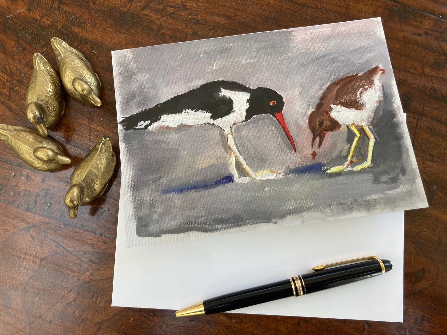 Mock up of Shore Birds Greeting card by Janet Lee Chauncey on table top with pen and brass duck figurines.