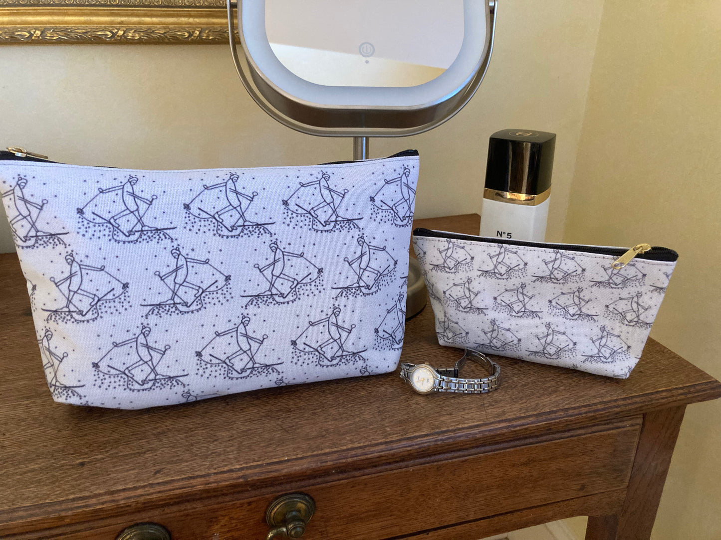 Two accessory bags with skier pattern on a wooden surface next to a mirror.