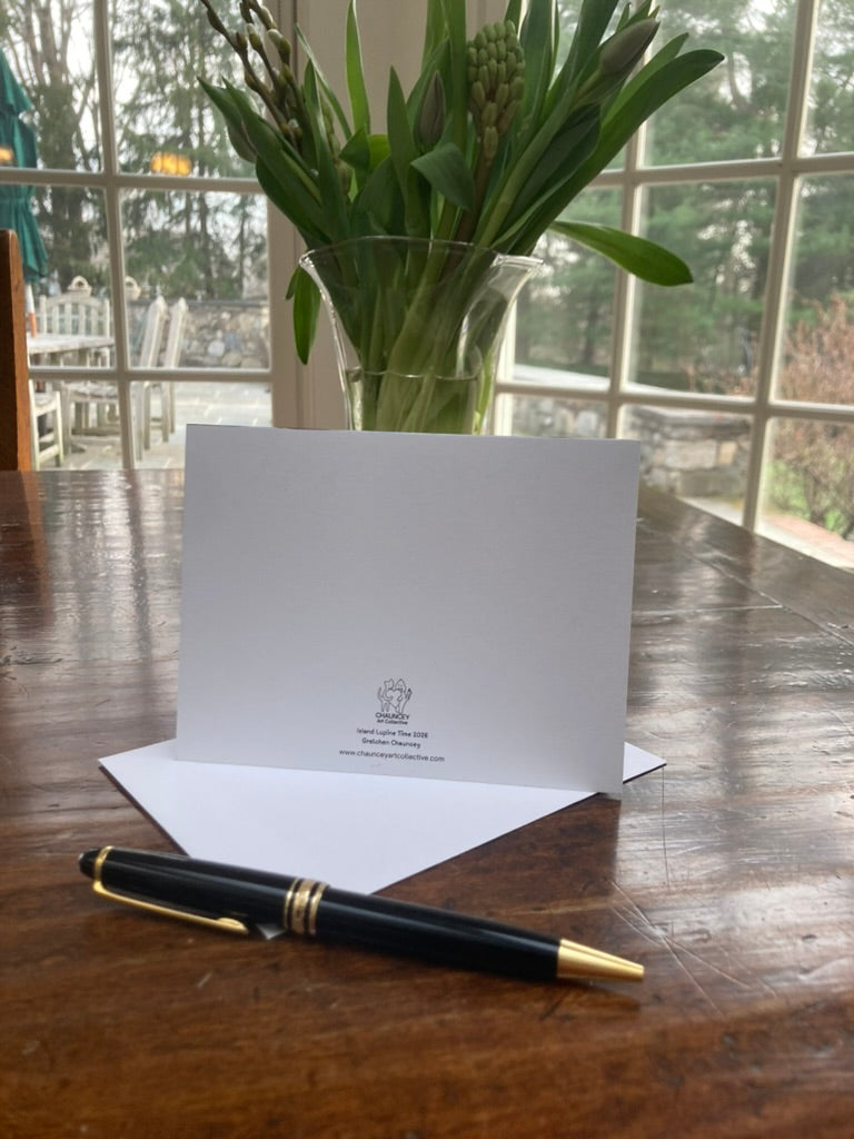 Back side of white card with a pen and vase of flowers on a wooden table
