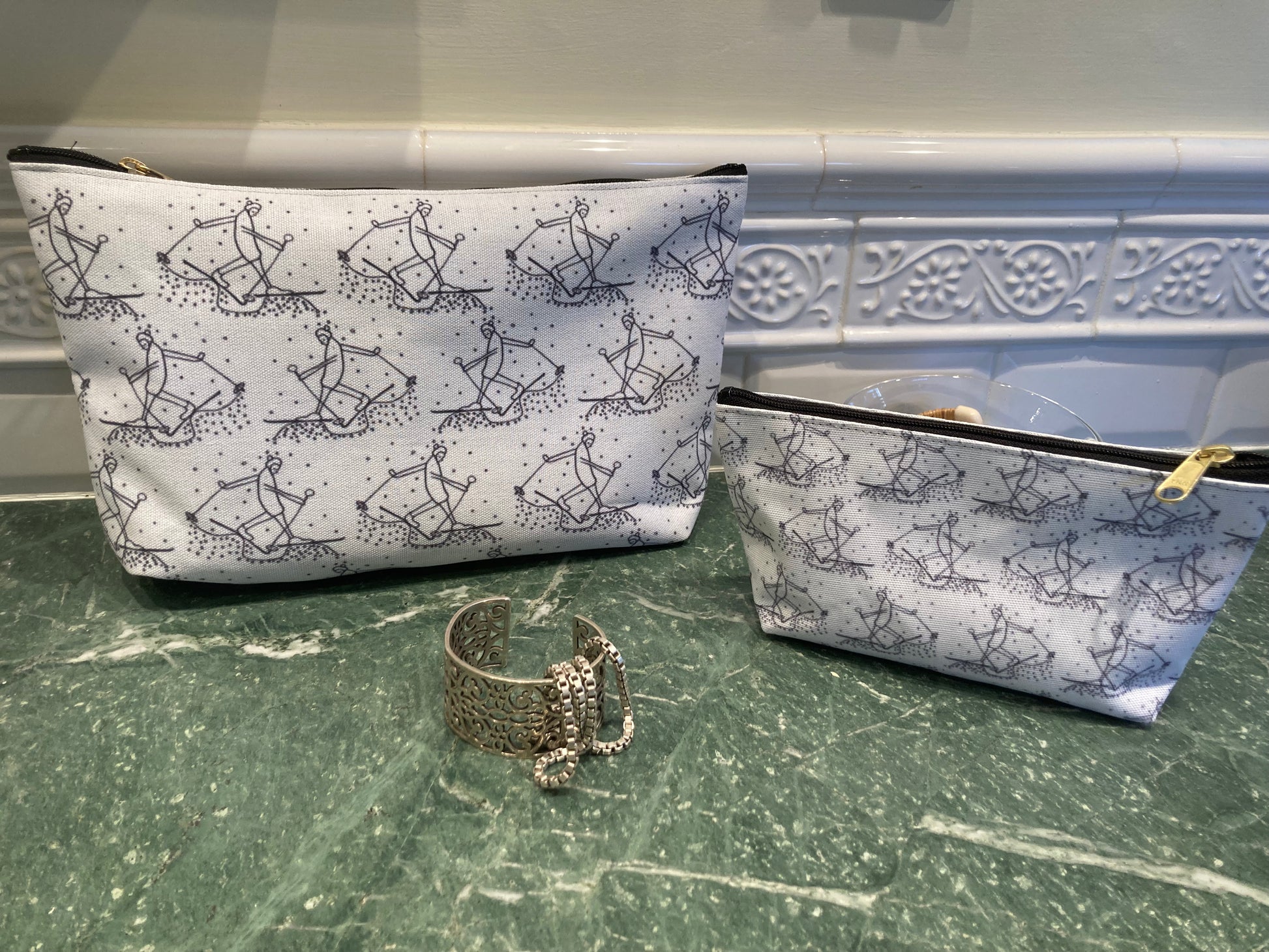 Trail Blazer pouches with cross country skier in black pen on white border resting on marble counter with silver bracelet and necklace.