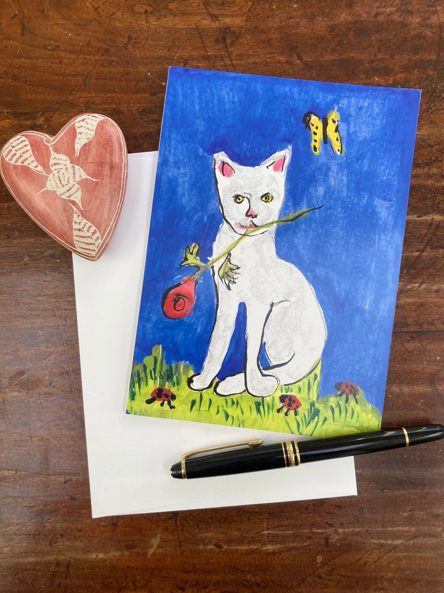 Caspar and Suddenly greeting card with a cat illustration on a wooden surface with a pen and heart-shaped object.