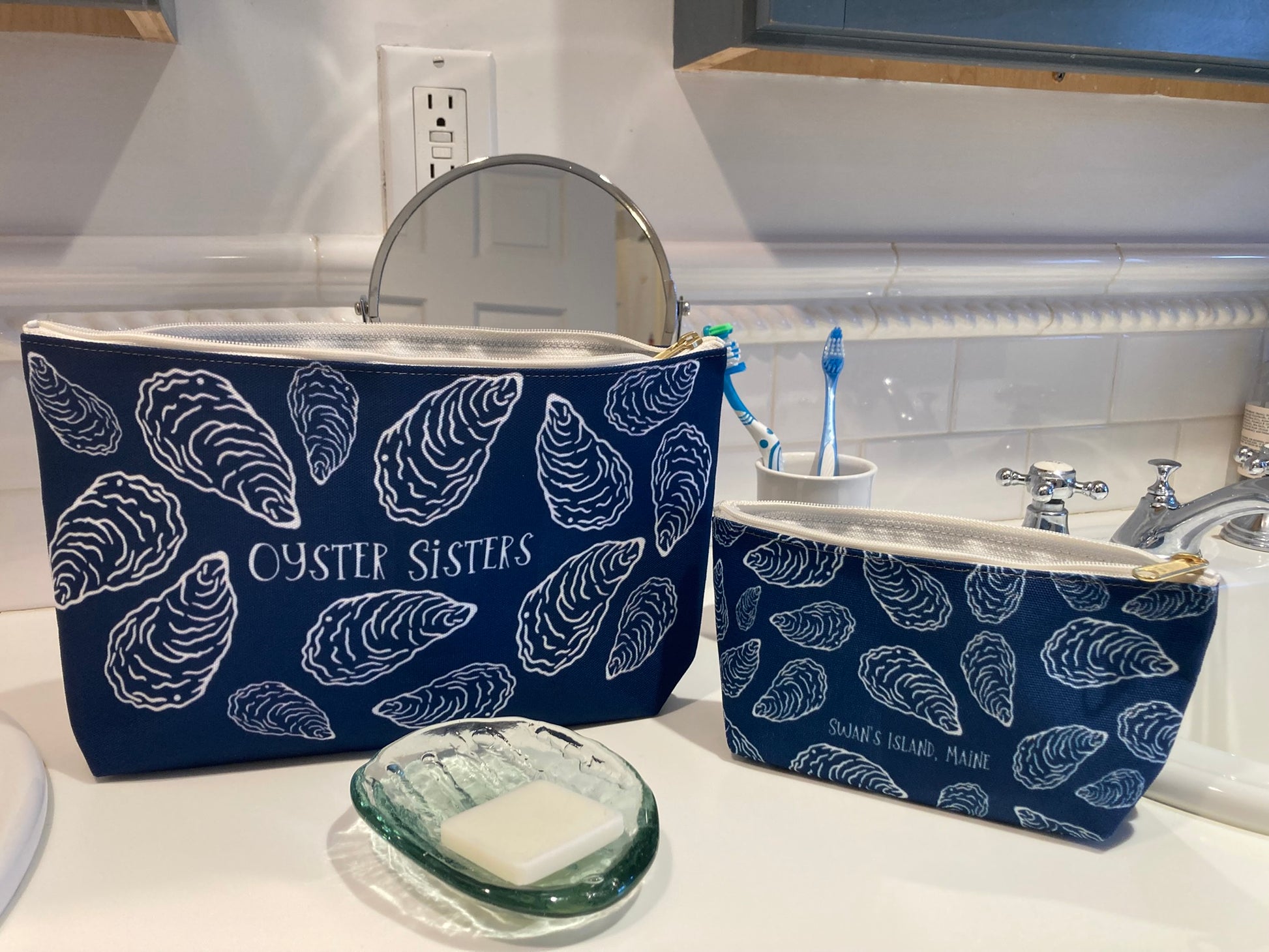 Two blue cosmetic bags with white shell pattern on a bathroom counter.