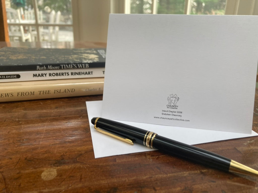 Pen and back of the greeting card showing title and logo with envelope on a wooden surface with books in the background