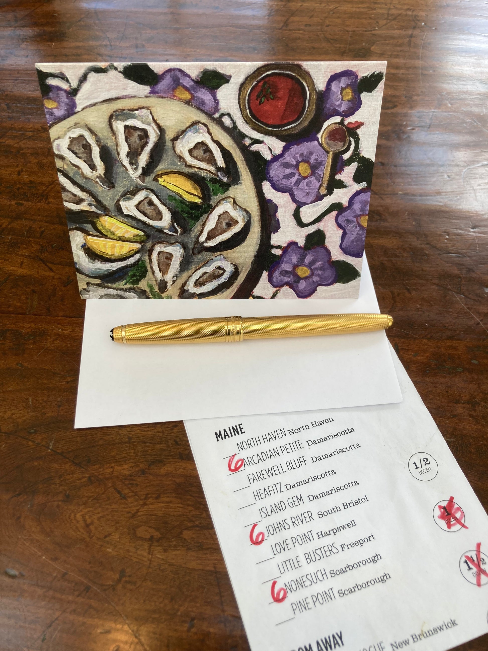 Oyster Sisters Social greeting card with art work by Gretchen Chauncey displayed on table top with pen and list of types of oysters.