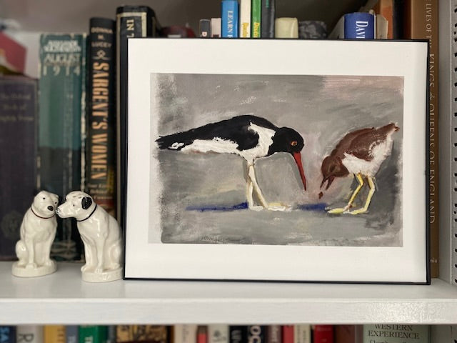 Framed artwork of two birds on a shelf with decorative dog figurines and books.