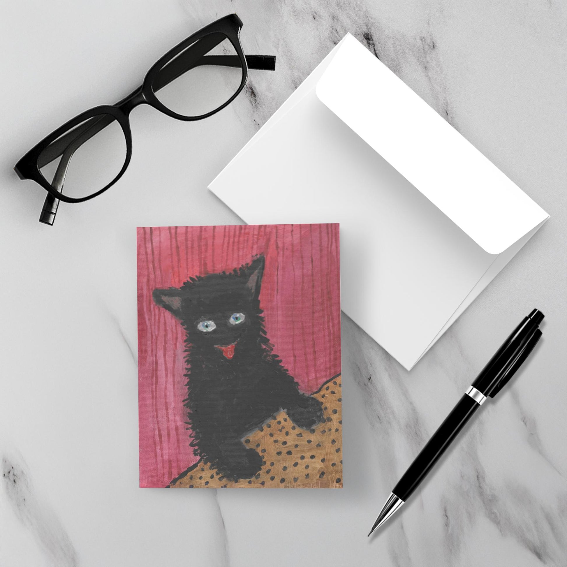 The all occasion greeting card Happy Cat is sitting on a marble surface next to the envelope, a black pen and reading glasses.