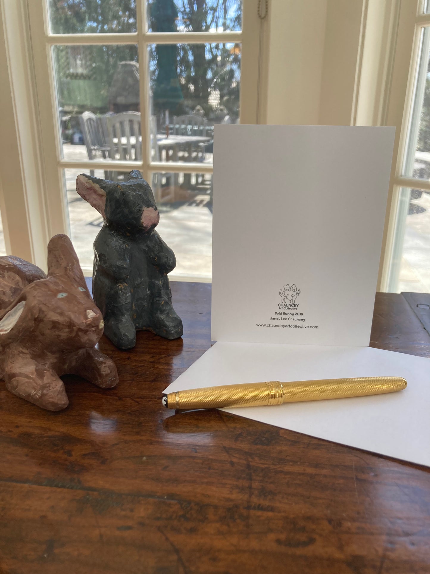 Two Easter bunny figurines and a gold pen on a wooden table with the back of the Bold Bunny card