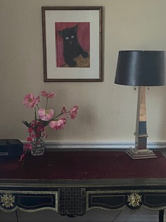 Happy Cat art print hangs on the wall above a desk with a lamp and a vase of flowers. Art print by Chauncey Art Collective.