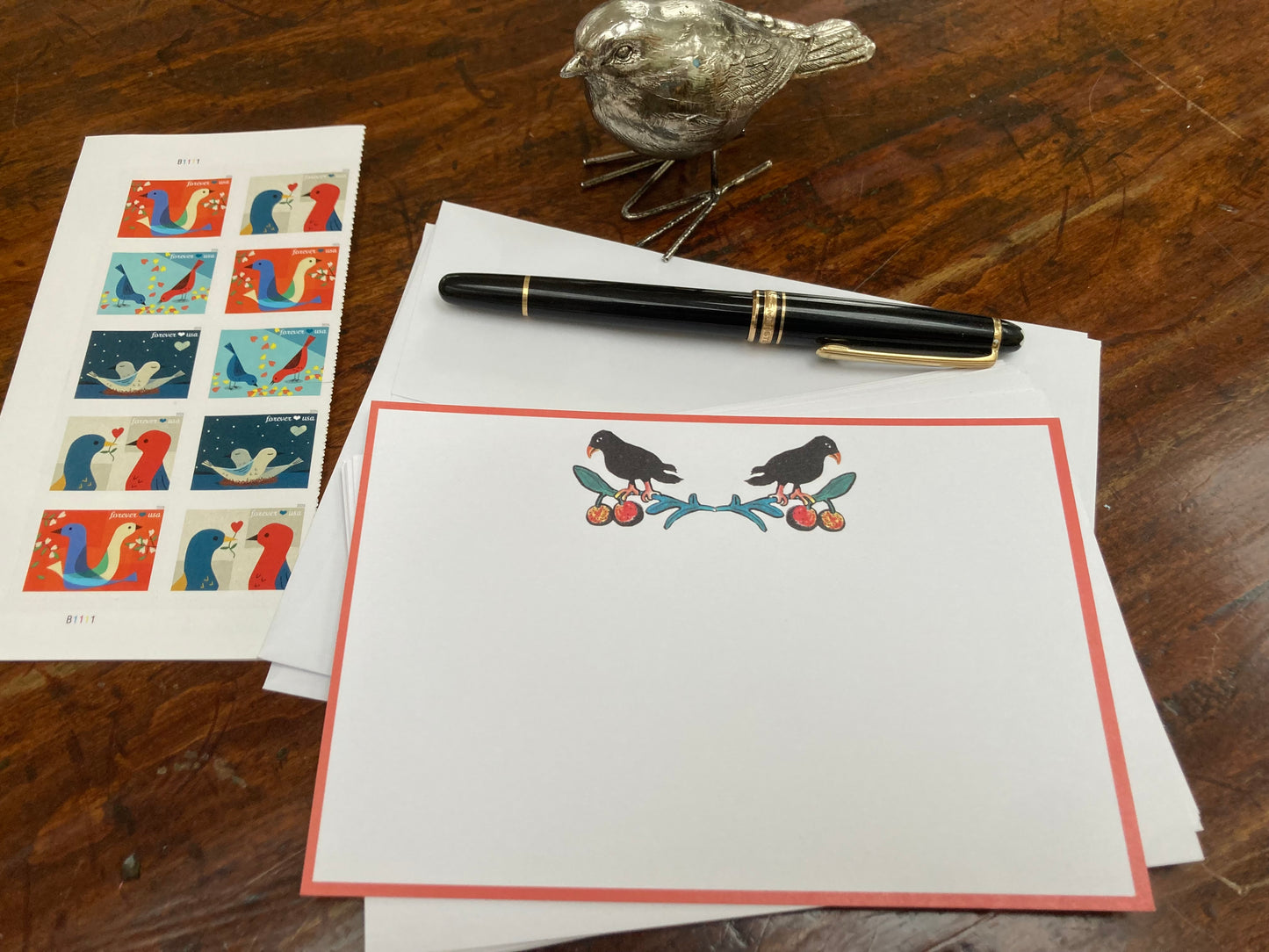Stationery set with a pen, stamps, and a decorative bird on a wooden surface