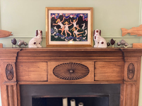Mockup of River Dancing art print over a wooden mantelpiece surrounded by brown and white Staffordshire dogs and  silver birds.