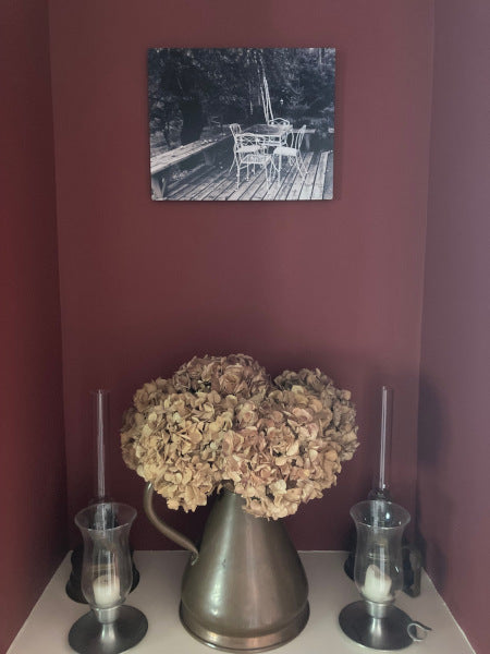 Mockup of the metal print shown hanging on a burgundy colored wall above a large dried hydrangea flower and two antique brass candlesticks.