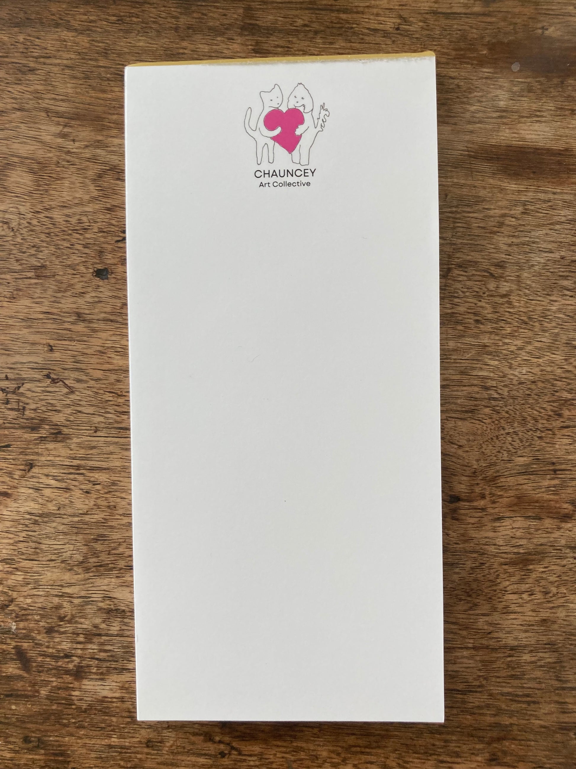 A mockup of the Chauncey Art Collective logo magnetic notepad atop wooden table.