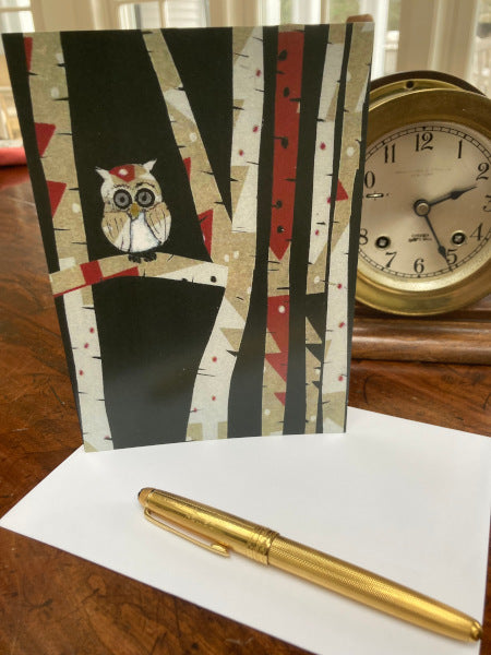 Mockup of greeting card Owl In Trees with its envelope and a gold pen on a wooden desk with a ship clock.
