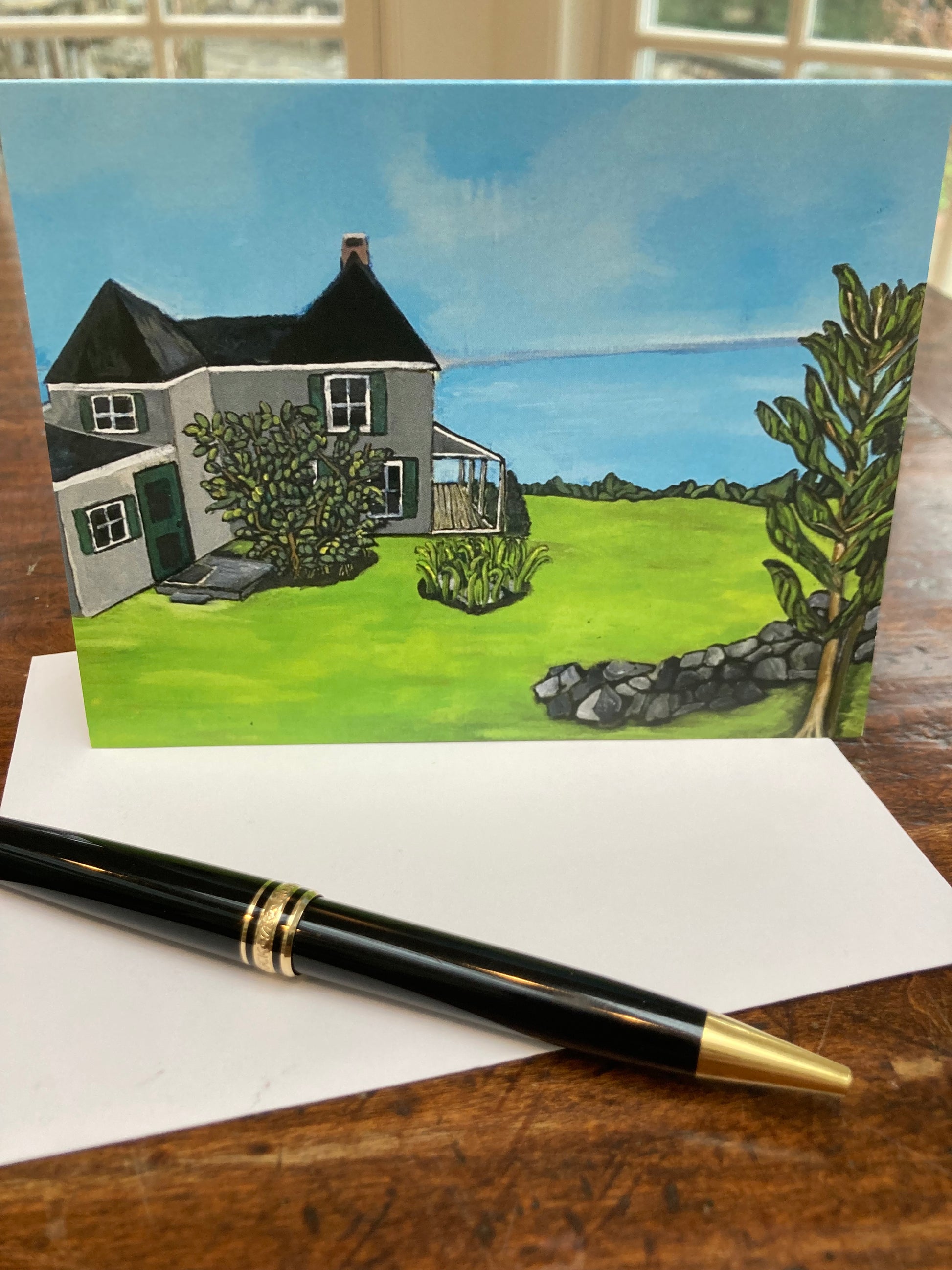 Mockup of Nutshell Cottage greeting card on a wooden table which highlight the greens and blues in the card.
