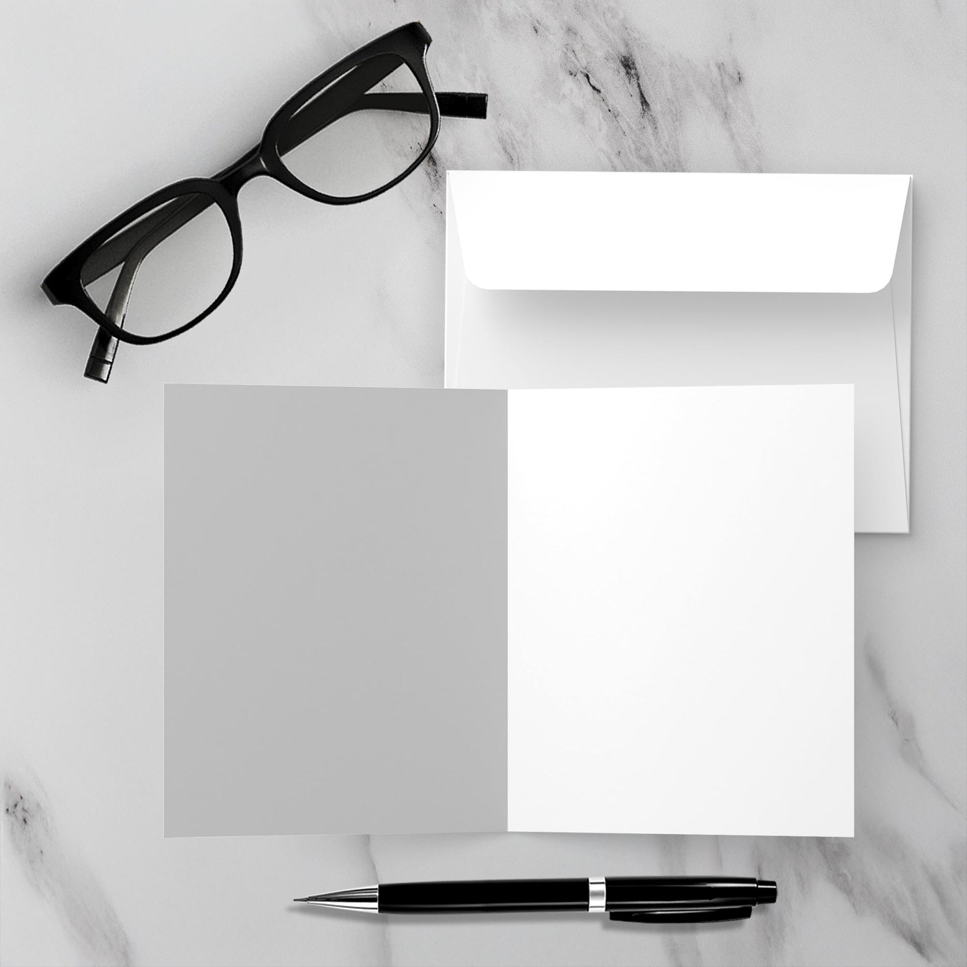 Mock up showing the blank inside of the greeting card Home Sweet Home along with the envelope. The background is a white marble surface with a black pen and reading glasses.