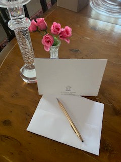 The mock up on the dining room table with the crystal candlestick and vase with miniature roses now showcases the rear of the birthday card, its envelope and a gold pen.