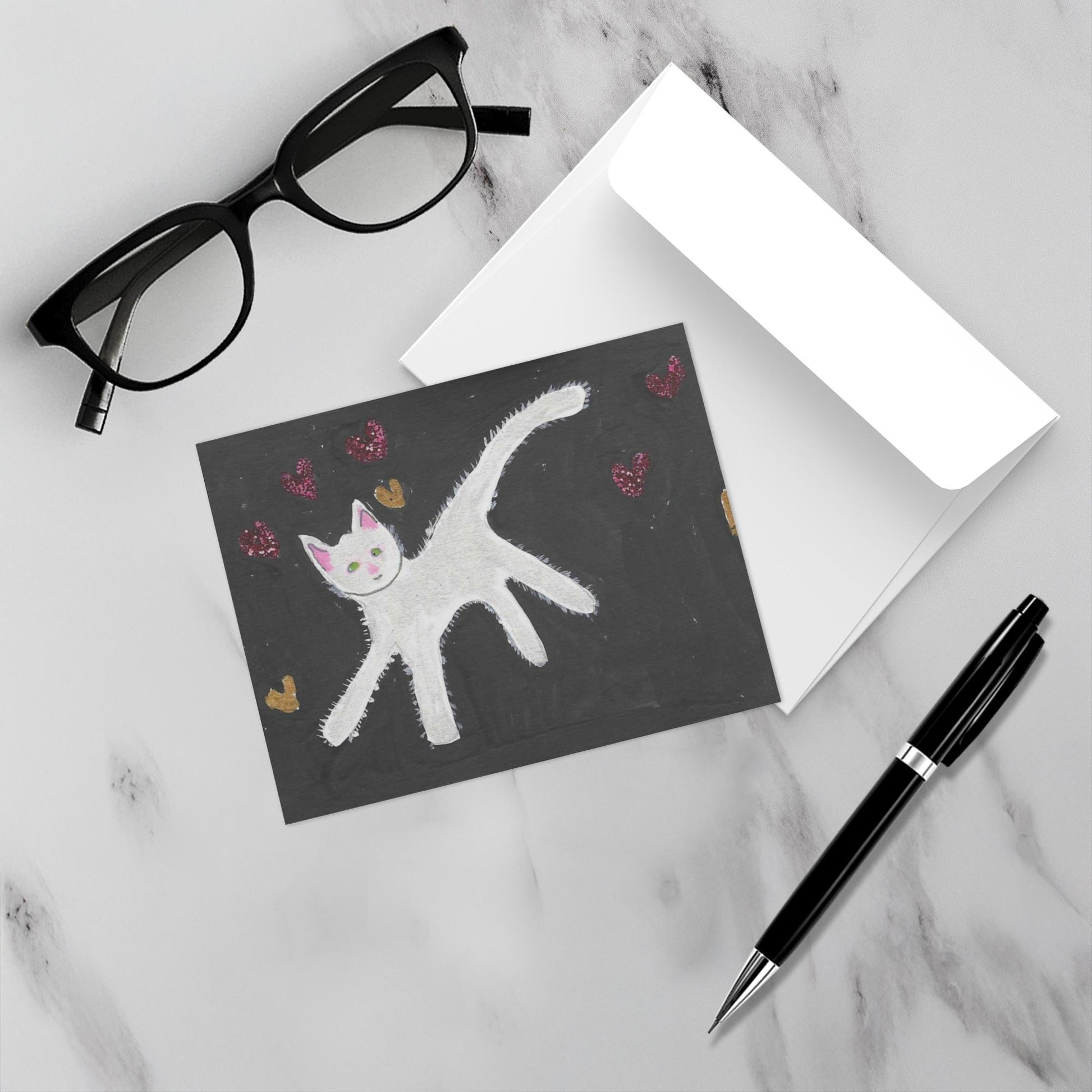 Mockup display showcasing the front of the greeting card Caspar With Floating Hearts lying on a gray marble surface along side a white envelope, a pair of black reading glasses and a black pen.