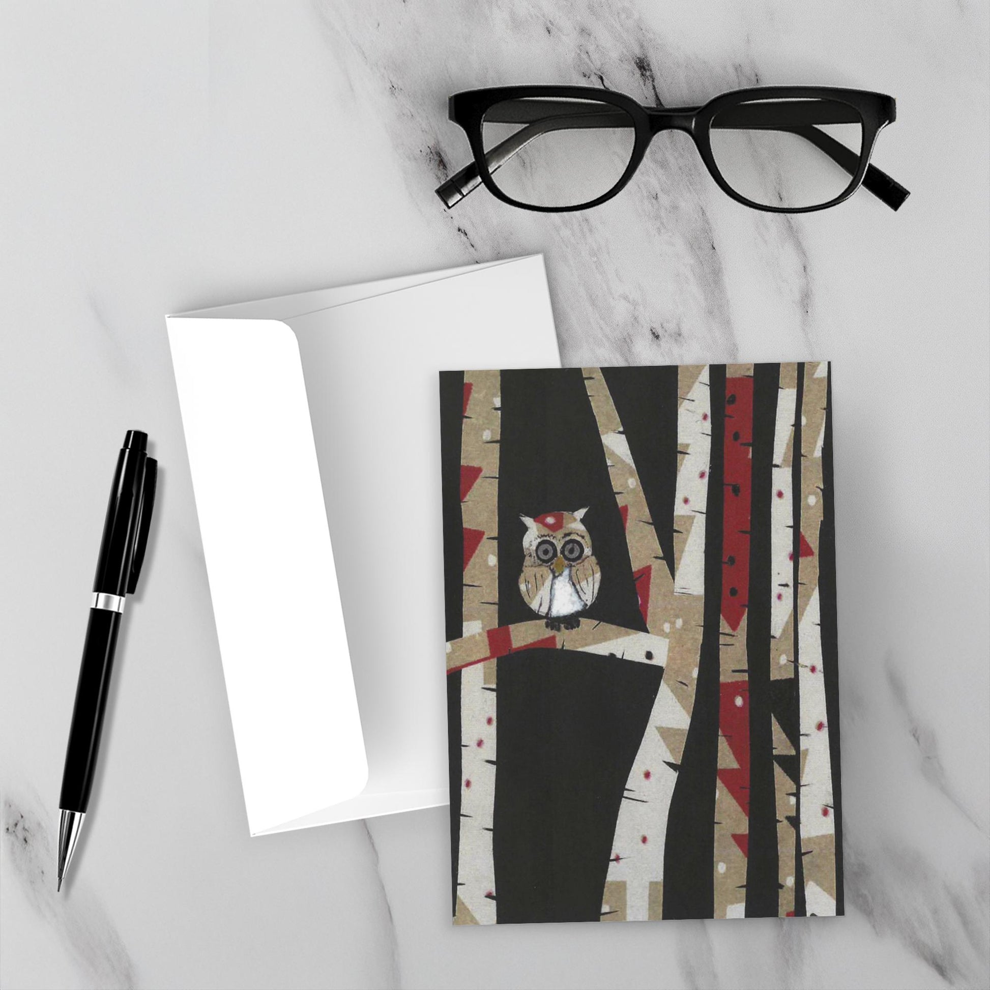 Mock up of the cute Owl In Trees greeting card set on a white marble backdrop with its envelope and a black pen and reading glasses.