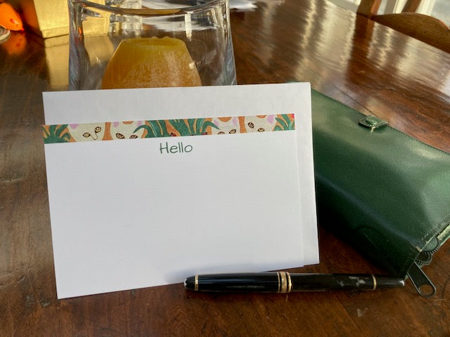 Note card with cat and foliage border and Hello text on a wooden surface with a pen and green case.
