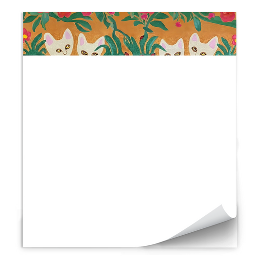 Set against an ochre background 4 adorable white cats peer out to look at you. They are partially hidden behind green leaves and flowers, but there they are. Curious Cats notepad