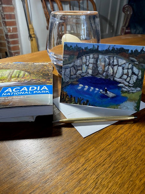 Eagle On Duty card shown with its envelope and a gold pen next to a book on Acadia on a wooden table.