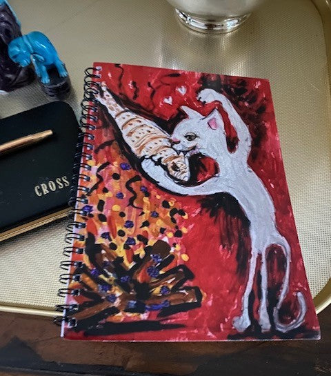Mockup of Firepit Fun! spiral notebook ready to be used on a table with a pen.
