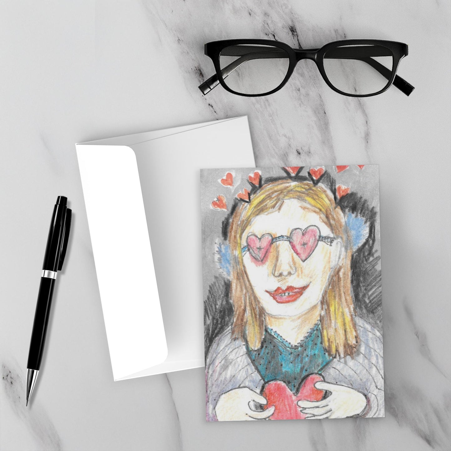 The front of the card is resting on a marble backdrop in this mock up with the envelope a black pen and reading glasses.