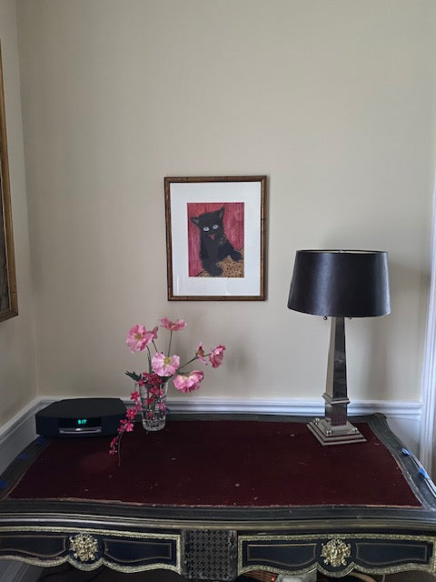Decorative setup with a framed picture of a Happy Cat, art print hanging above a vase with pink flowers,