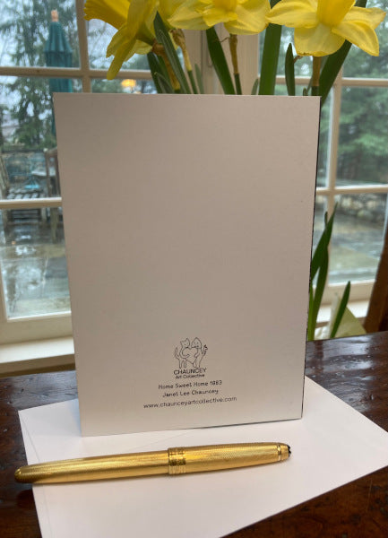 Mock up of the back of the greeting card Home Sweet Home showing Chauncey Art Collective's logo, a gold pen in front of a bouquet of daffodils