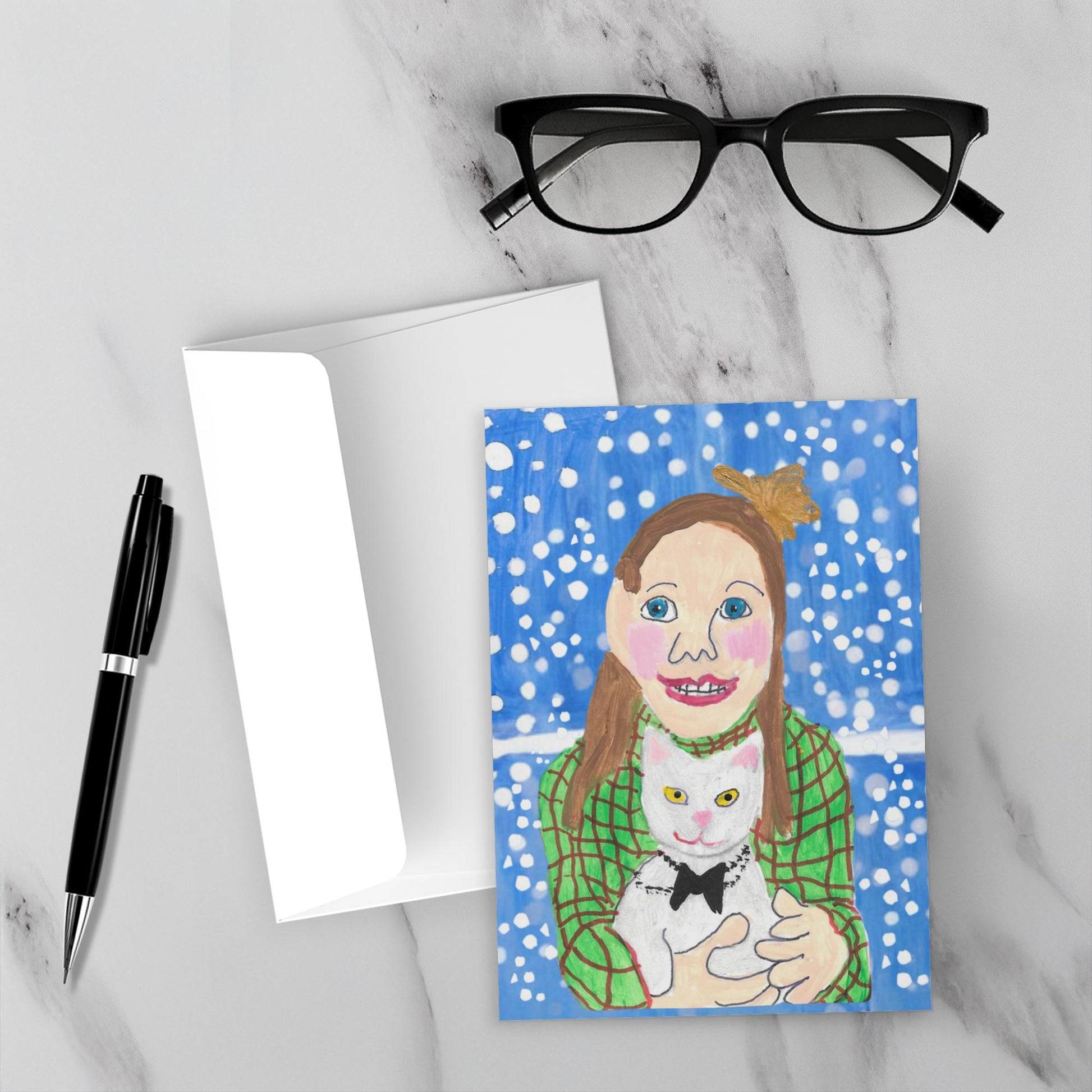 Card with a painting of a person holding a cat, placed on a marble surface with glasses and a pen.