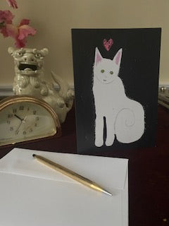 Mockup of the card on a burgundy velvet desk surrounded by a white foo dog statue, gold clock and the envelope.
