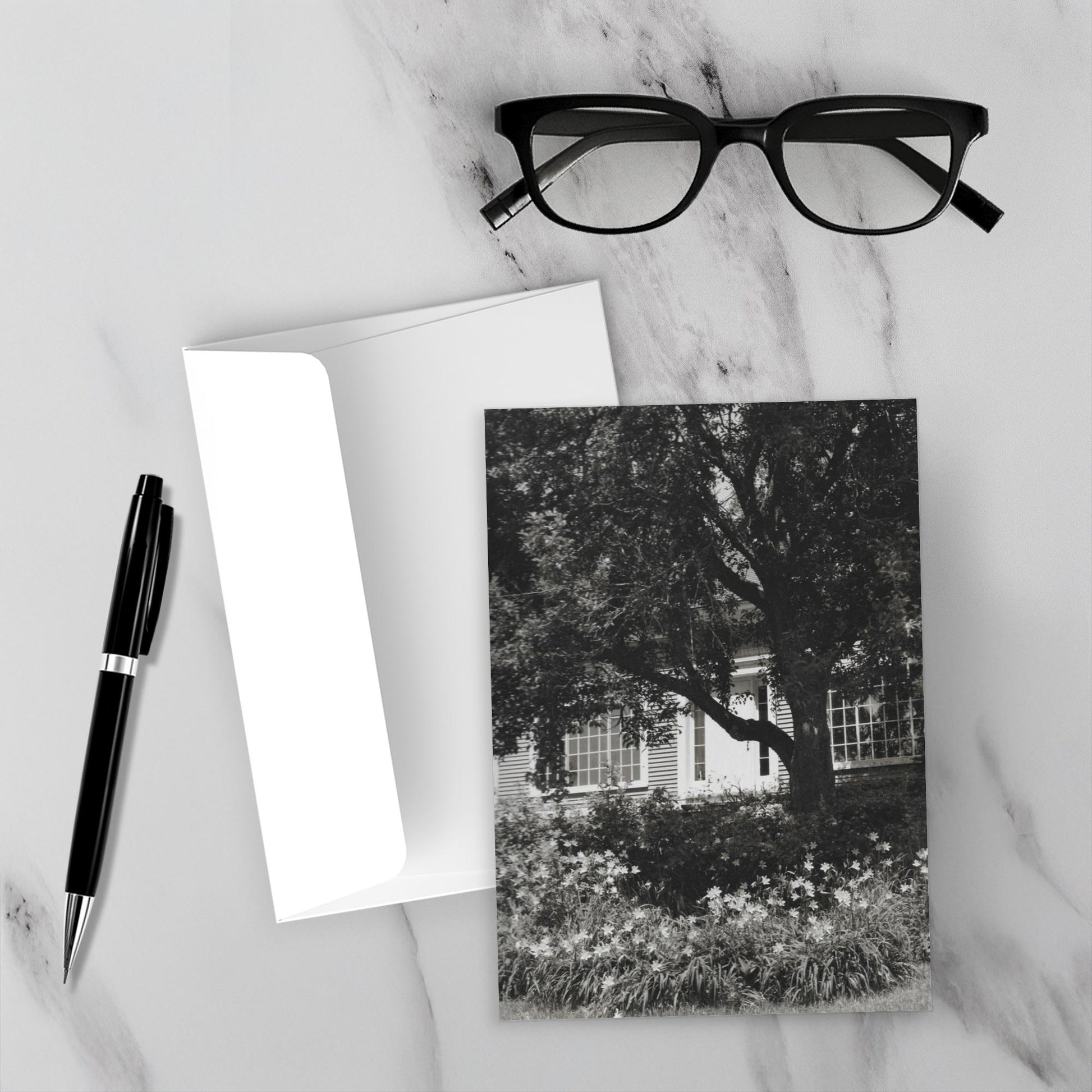 The front and back of the greeting card Home Sweet Home and the envelope surrounded by a black fountain pen and black reading glasses.