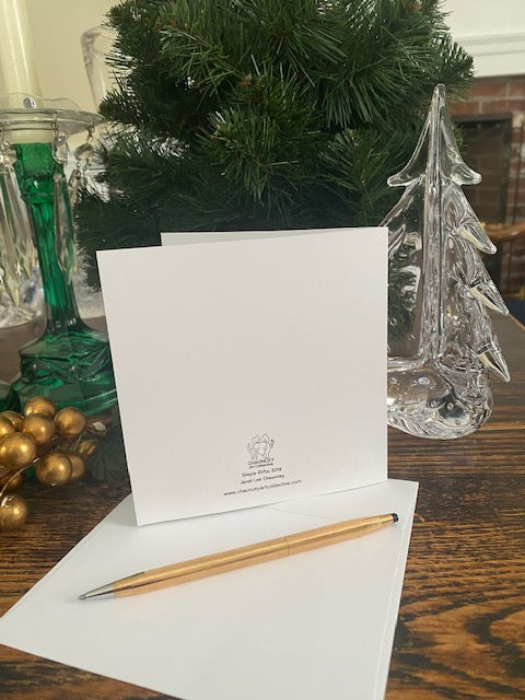The back of the greeting card with Chauncey Art Collective branding on a wooden surface with Christmas decorative elements